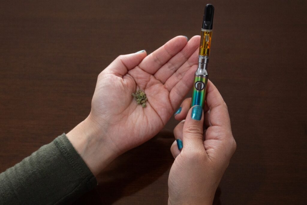 A woman holding a weed pen in her right hand and some THCA flower in her left hand